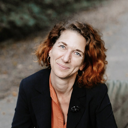 Dozentin mit roten Haaren lächelt in die Kamera.