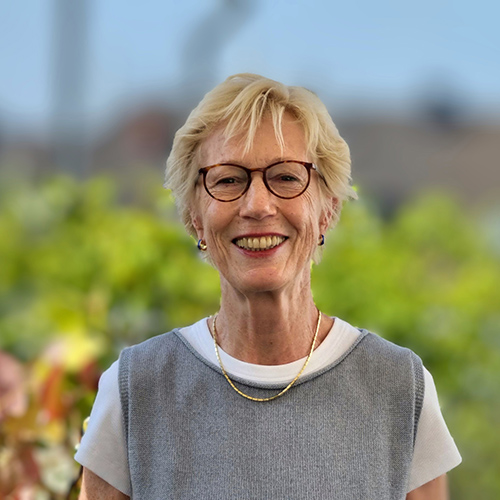 Dozentin mit blonden kurzen Haaren und Brille steht draußen in der Natur vor unscharfem Hintergrund